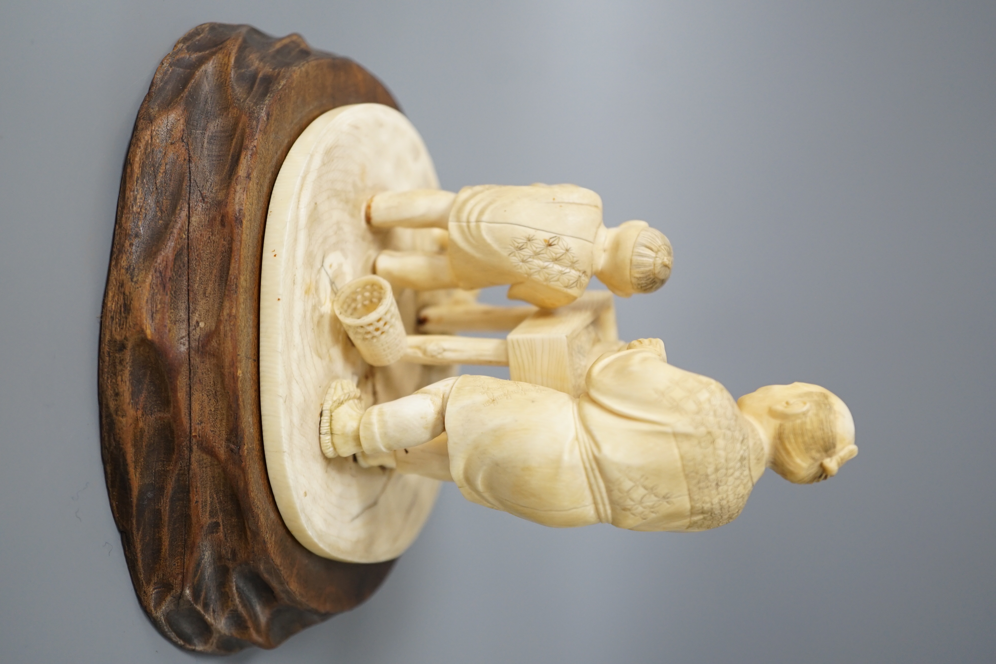 A Japanese ivory okimono of man and boy at a grindstone, Meiji period, signed, wood stand. 15cm total height